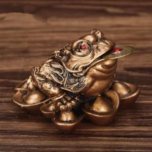 Figurine de grenouille au ton bronze assise sur des pièces et tenant un jeton rouge