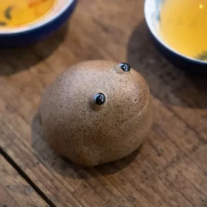 Petite figurine grenouille en céramique brune mouchetée près d’un service à thé