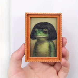 Petit cadre aimanté avec portrait fantaisie de grenouille verte tenu dans une main