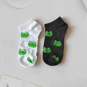 Une socquette blanche et une noire avec des motifs répétés de têtes de grenouille vertes